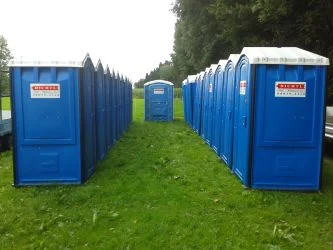 Zwei Reihen blauer Toilettenkabinen auf einer Wiese